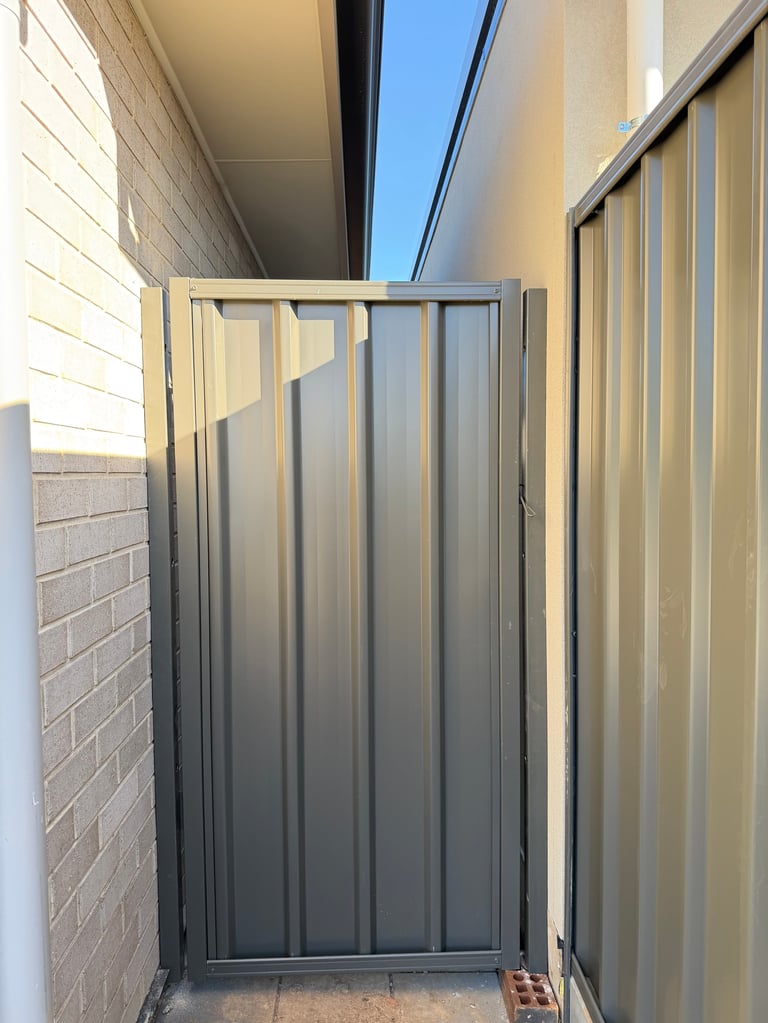Narrow outdoor space enclosed by brick walls and corrugated metal panels with a closed metal gate in the center
