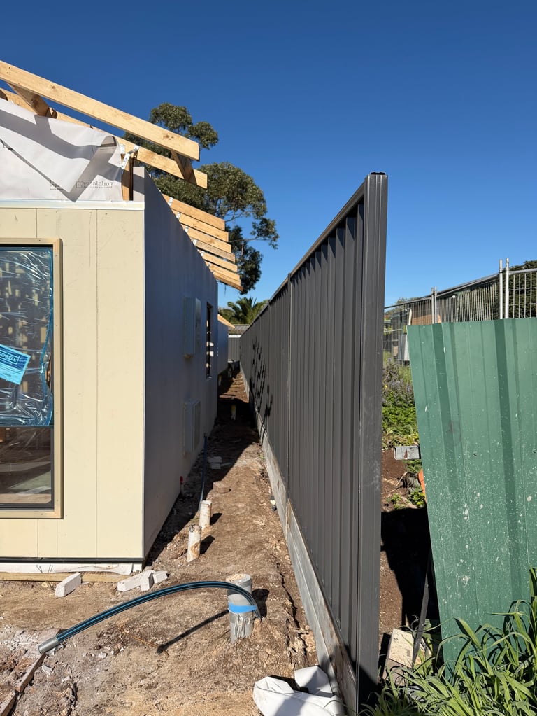 Narrow alleyway between cream and dark metal buildings under construction with clear blue sky overhead