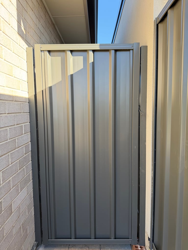 Gray metal corrugated gate installed between brick wall and light-colored exterior wall in narrow passage