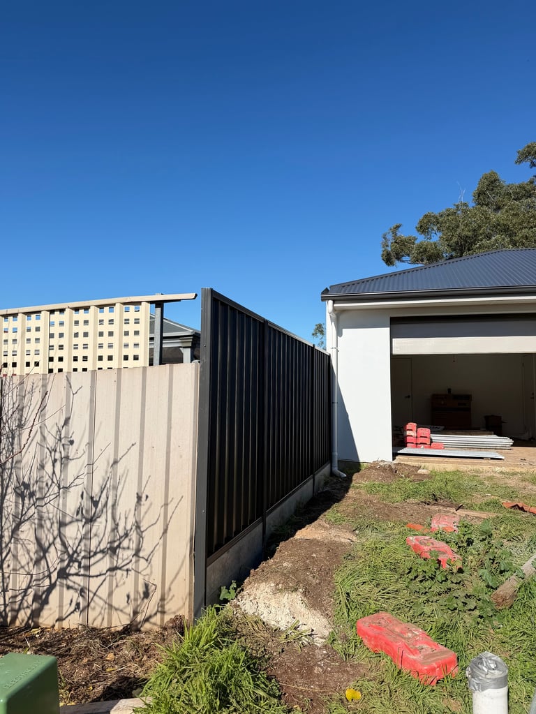 Backyard with metal fencing, white garage, bare tree, and red storage items under clear blue sky