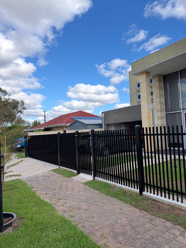Black metal fence and gate fronting a modern house with brick wall under blue sky with clouds